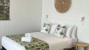 A neatly made bed with a patterned bedspread, white pillows with palm tree designs, and a round woven wall decoration.