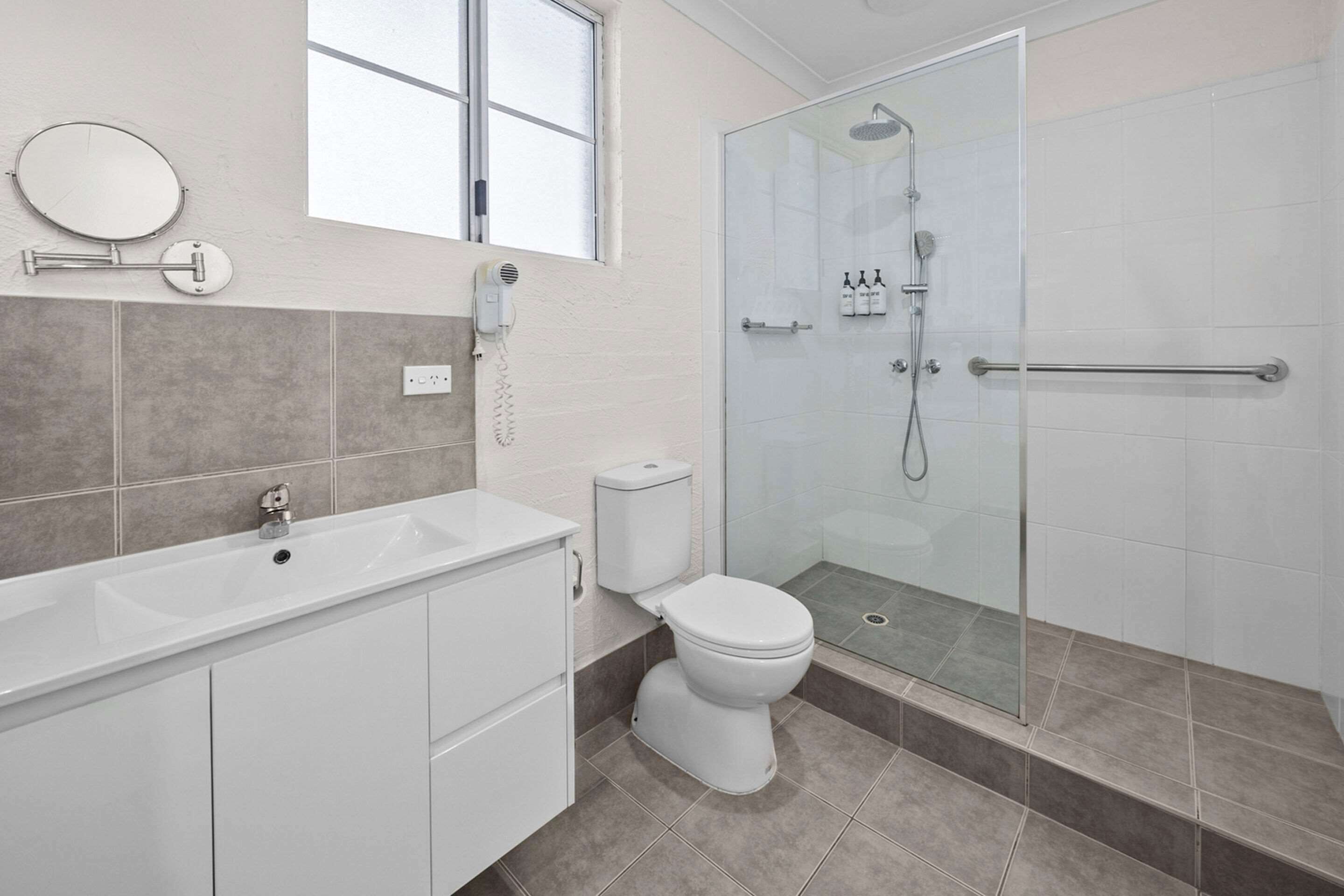 A modern bathroom with a white sink, toilet, and shower area.