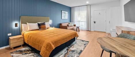 Un dormitorio moderno con una cama grande, una mesita de noche de madera, una mesita auxiliar, un sofá, una mesa de comedor y una silla.