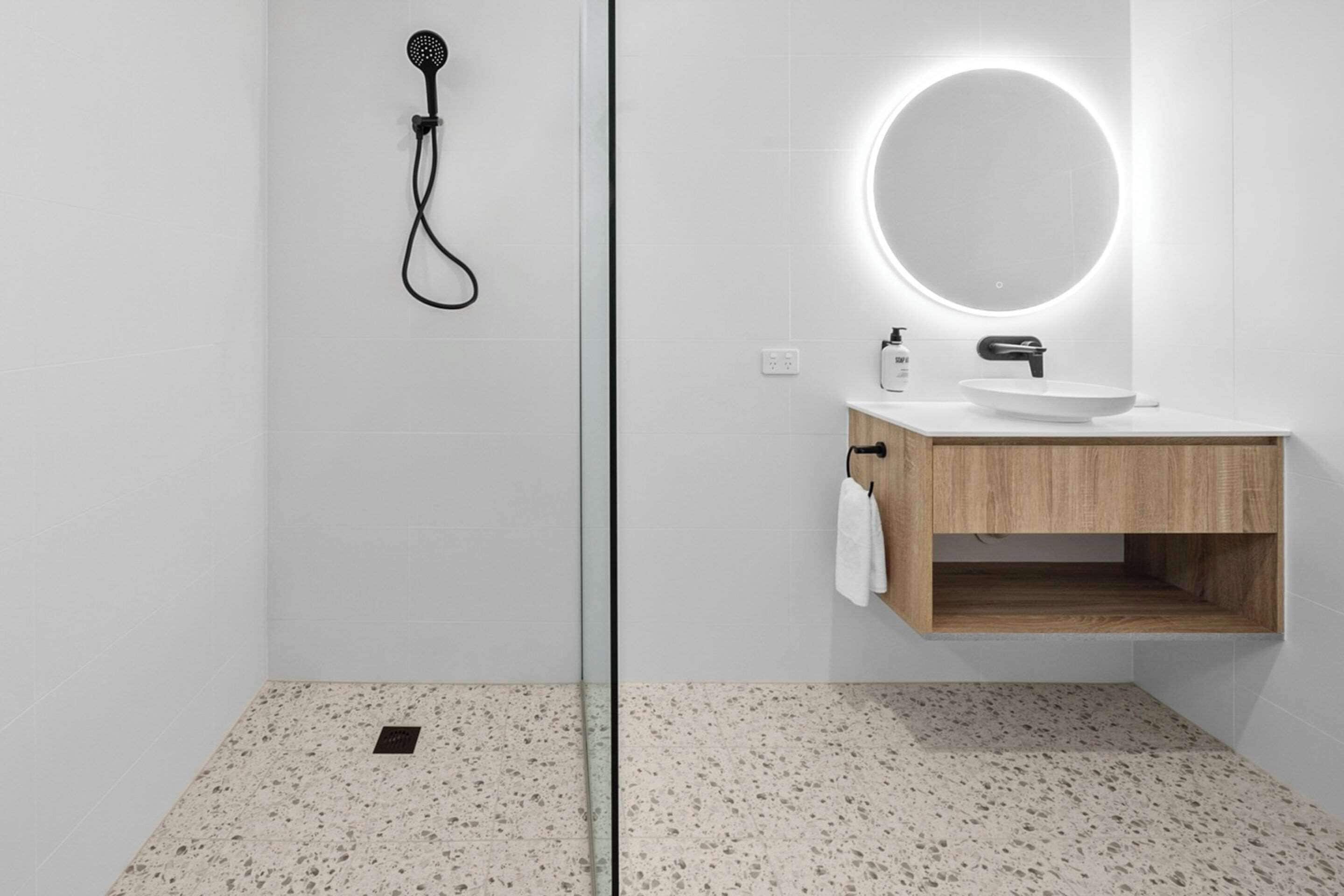 A modern bathroom with a shower, a sink with a round mirror, and a towel hanging on the wall.