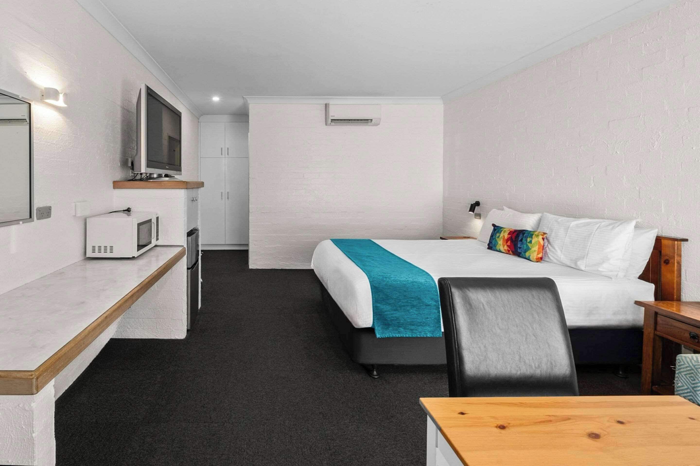 Una habitación de hotel con cama, escritorio con microondas, televisión y una mesita.