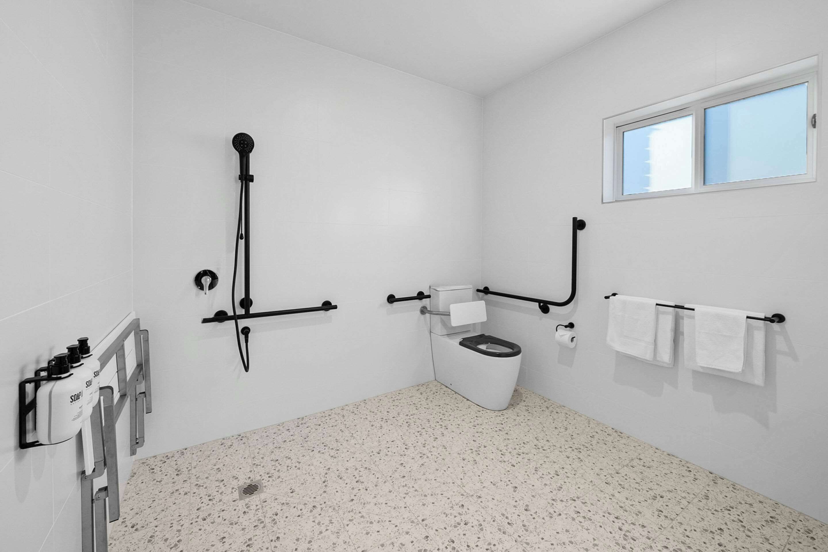 A modern bathroom with a toilet, bidet, and shower. There are towels on a rack and a window above the toilet.