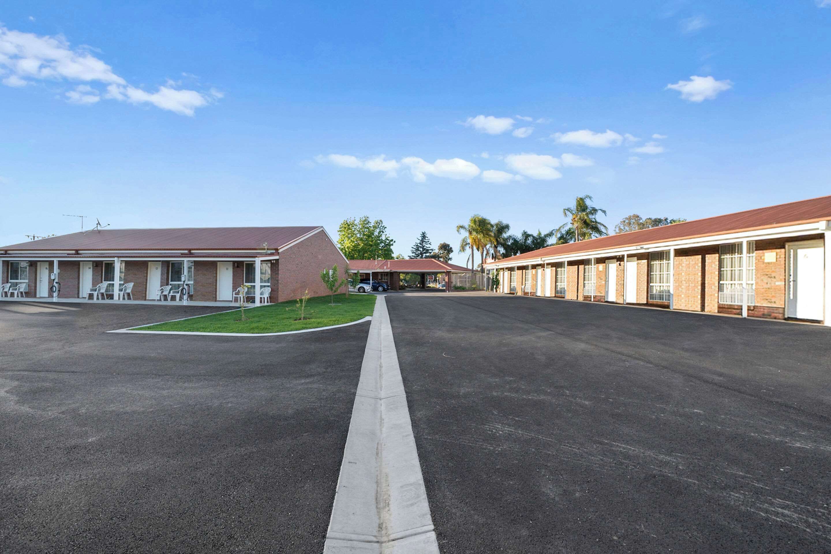 A motel with a central parking area, a small grassy patch, and a row of rooms with brick facades and white-framed windows.