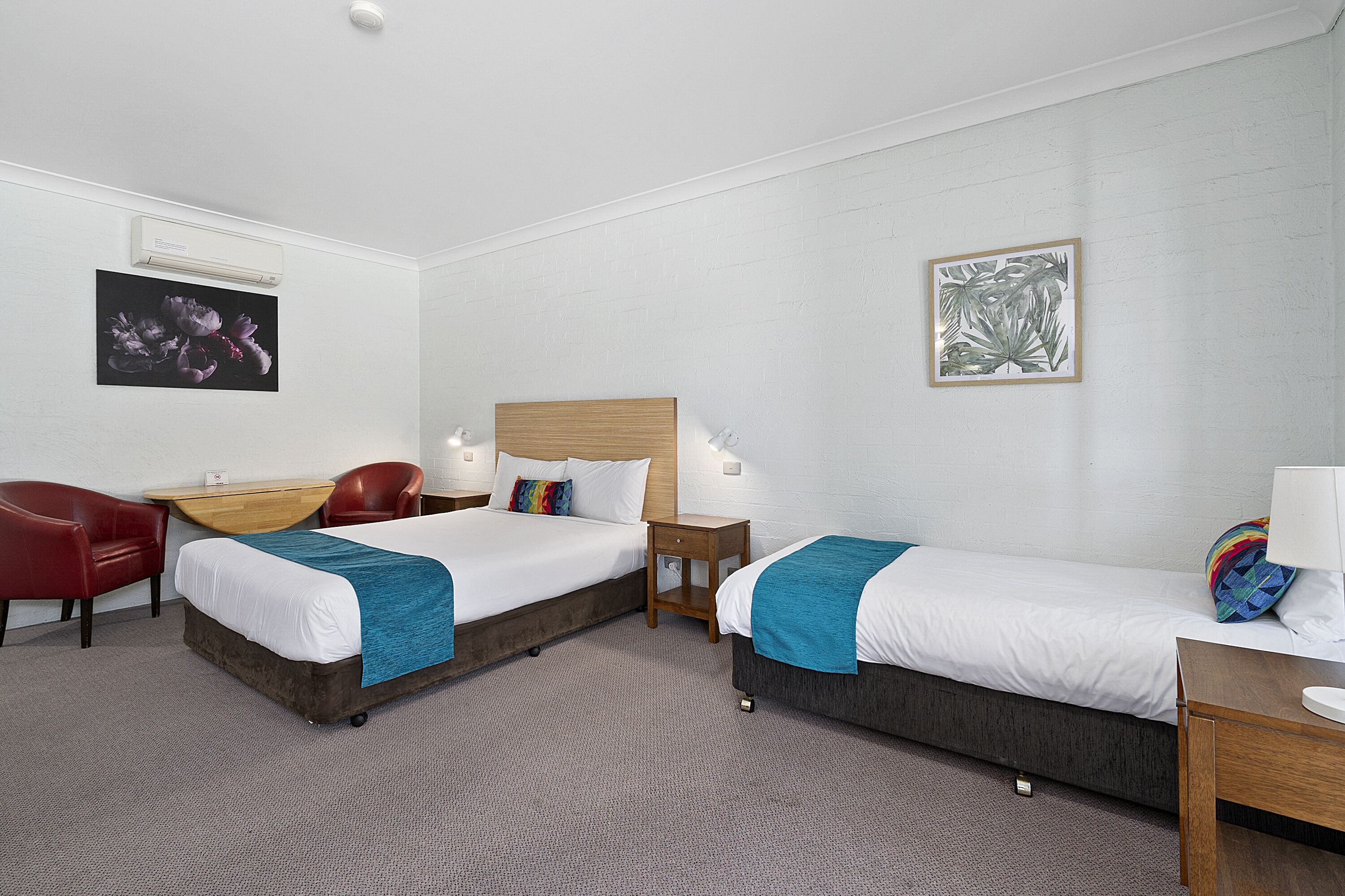 Ein Hotelzimmer mit zwei Betten, einem Schreibtisch, einem Stuhl und Bildern an der Wand.