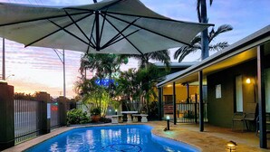 A swimming pool with a brick border, surrounded by a fence and potted plants. - Rockhampton Palms Motor Inn (Rockhampton)