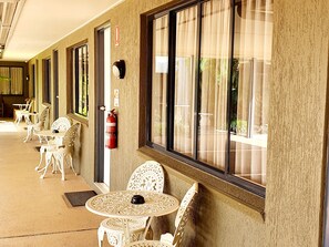 A corridor with white chairs and tables, a fire extinguisher, and a window with curtains.