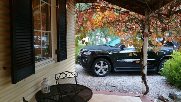 A covered porch with a table and chairs, a parked SUV, and a window with shutters. - Amy's House (Auburn)