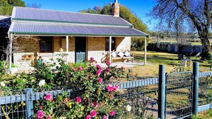 A stone house with a metal roof, a porch with a bench, and a garden with pink flowers. - Amy's House (Auburn)