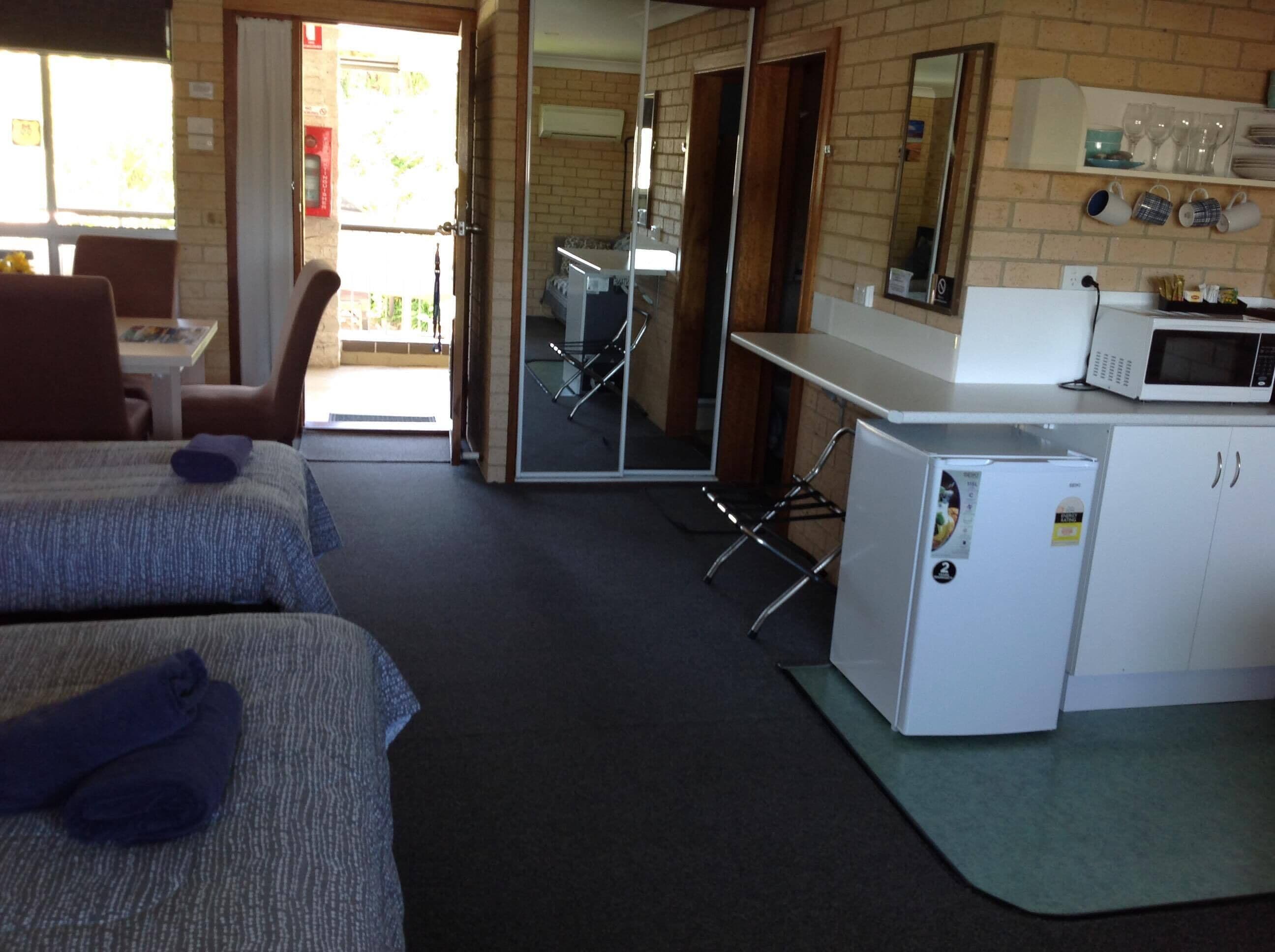Habitación de hotel con dos camas, kitchenette, comedor y puerta corrediza de vidrio al exterior.