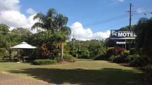 A motel with a large sign, a covered picnic area, and lush greenery.