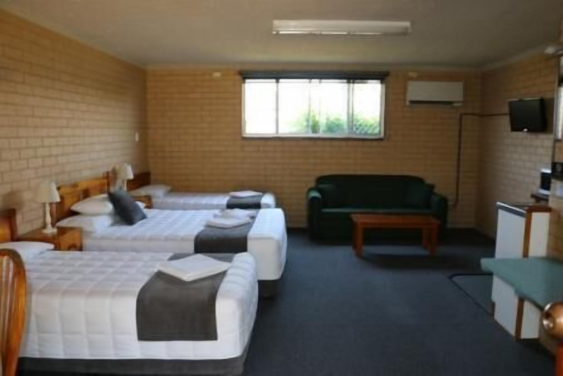A room with two beds, a green sofa, a small table, and a TV on the wall.