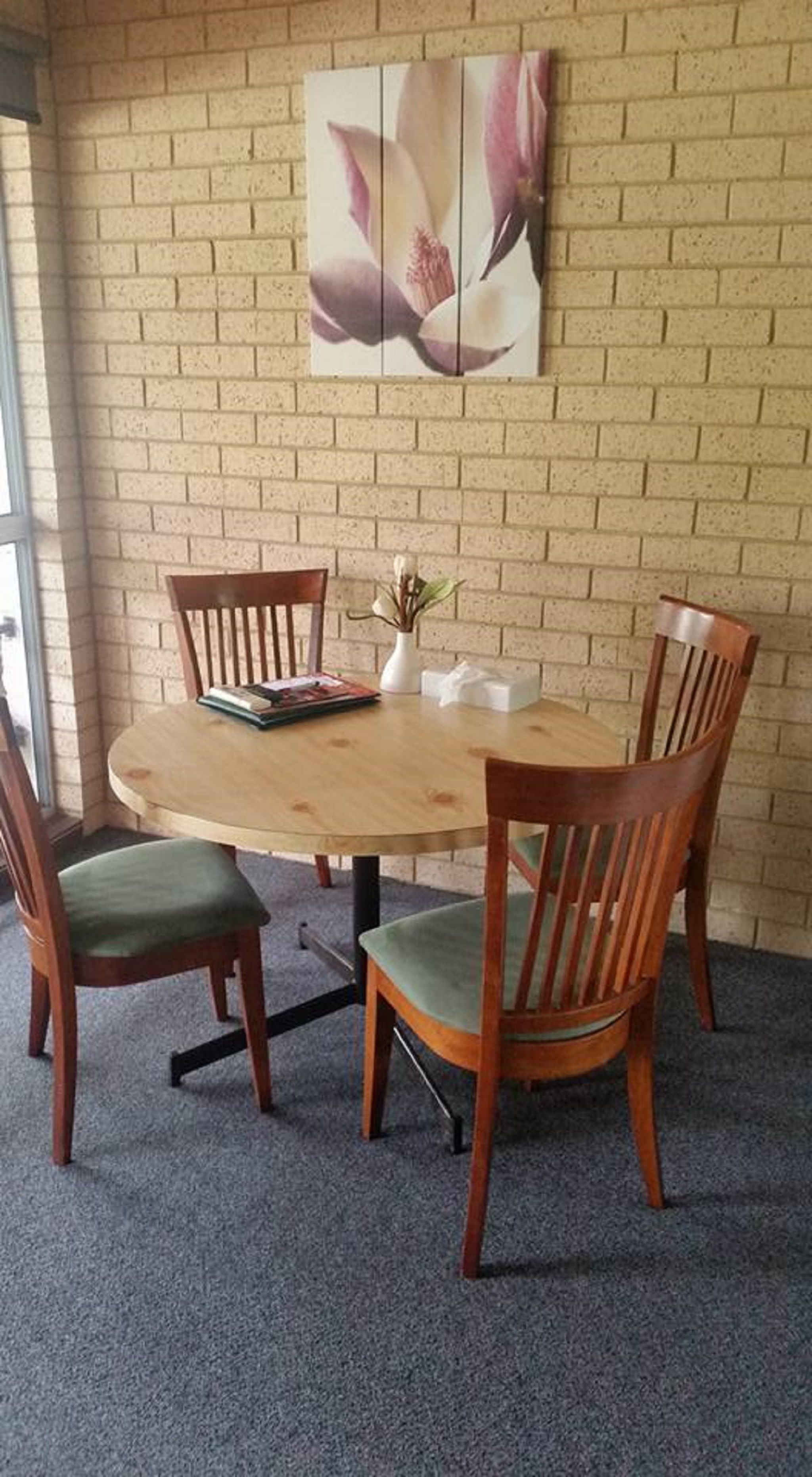 Una mesa redonda de madera con cuatro sillas, un florero con una planta y un cuadro de flores en la pared.