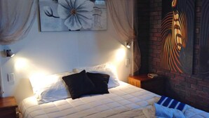 A bedroom with a large bed, two bedside lamps, a wall-mounted painting, and a brick wall.