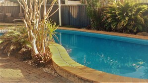 A swimming pool with a curved edge, surrounded by plants and a wooden fence.