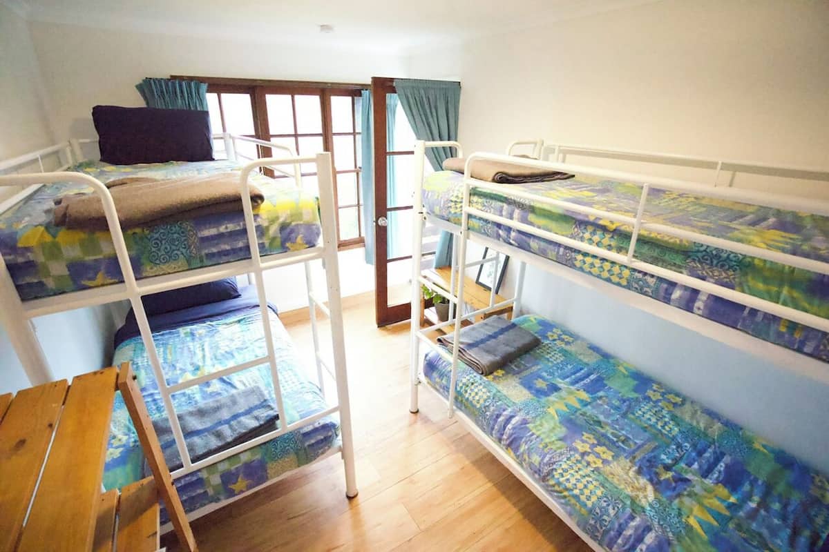 A dormitory room with bunk beds, wooden furniture, and a window with curtains.