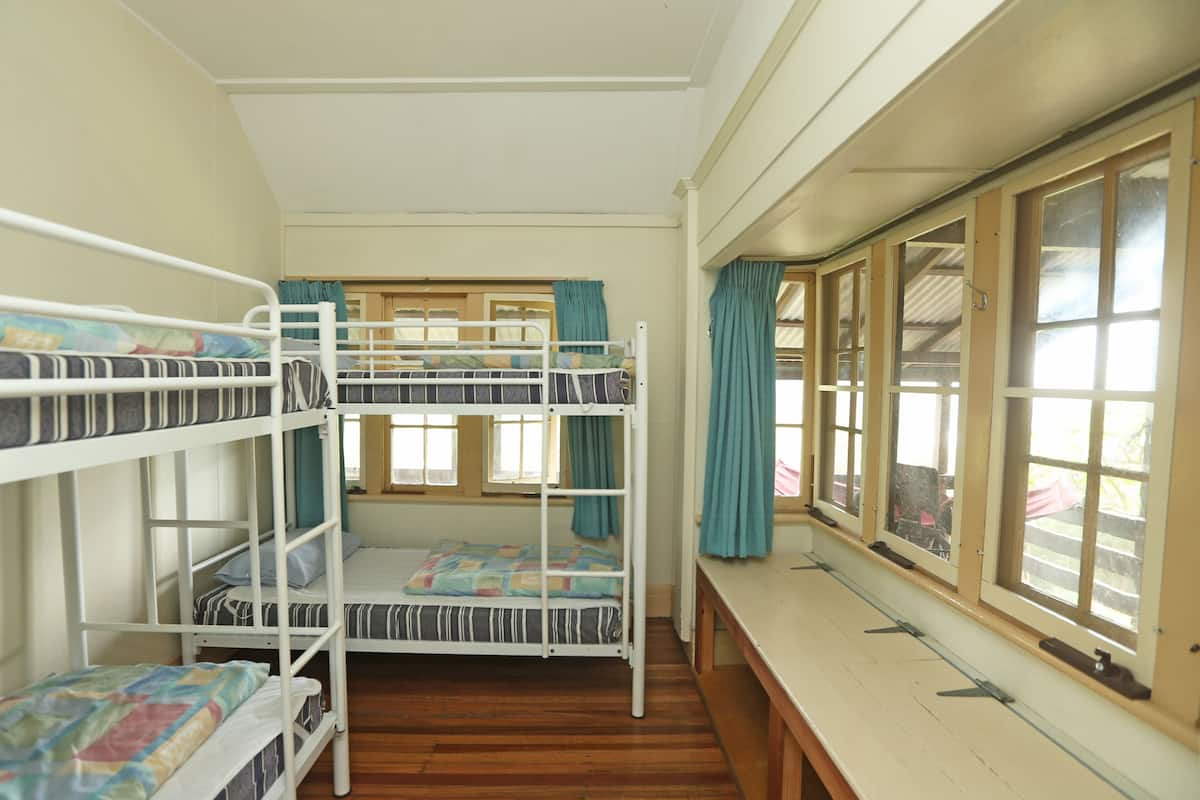 A bunk bed room with a wooden floor, a window with curtains, and a bench.