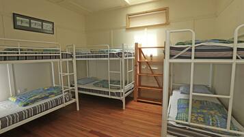A dormitory room with three bunk beds, wooden flooring, and a window with blinds.