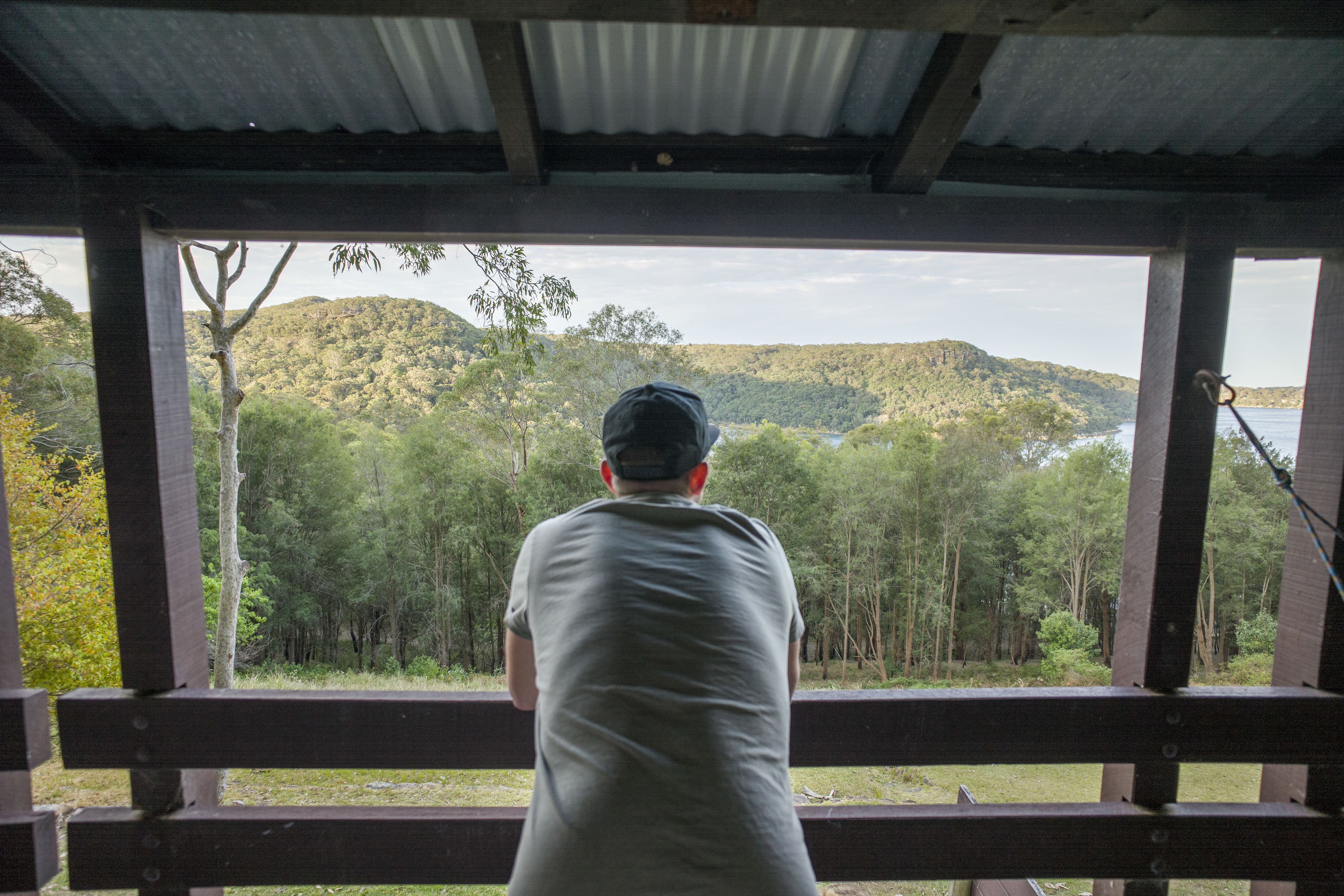 Une personne est assise sur un banc en bois, d’où elle a une vue sur une colline boisée et un plan d’eau.