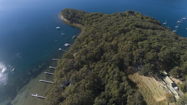 Vista aérea de una zona costera con denso bosque, un cuerpo de agua cristalina y varias embarcaciones.