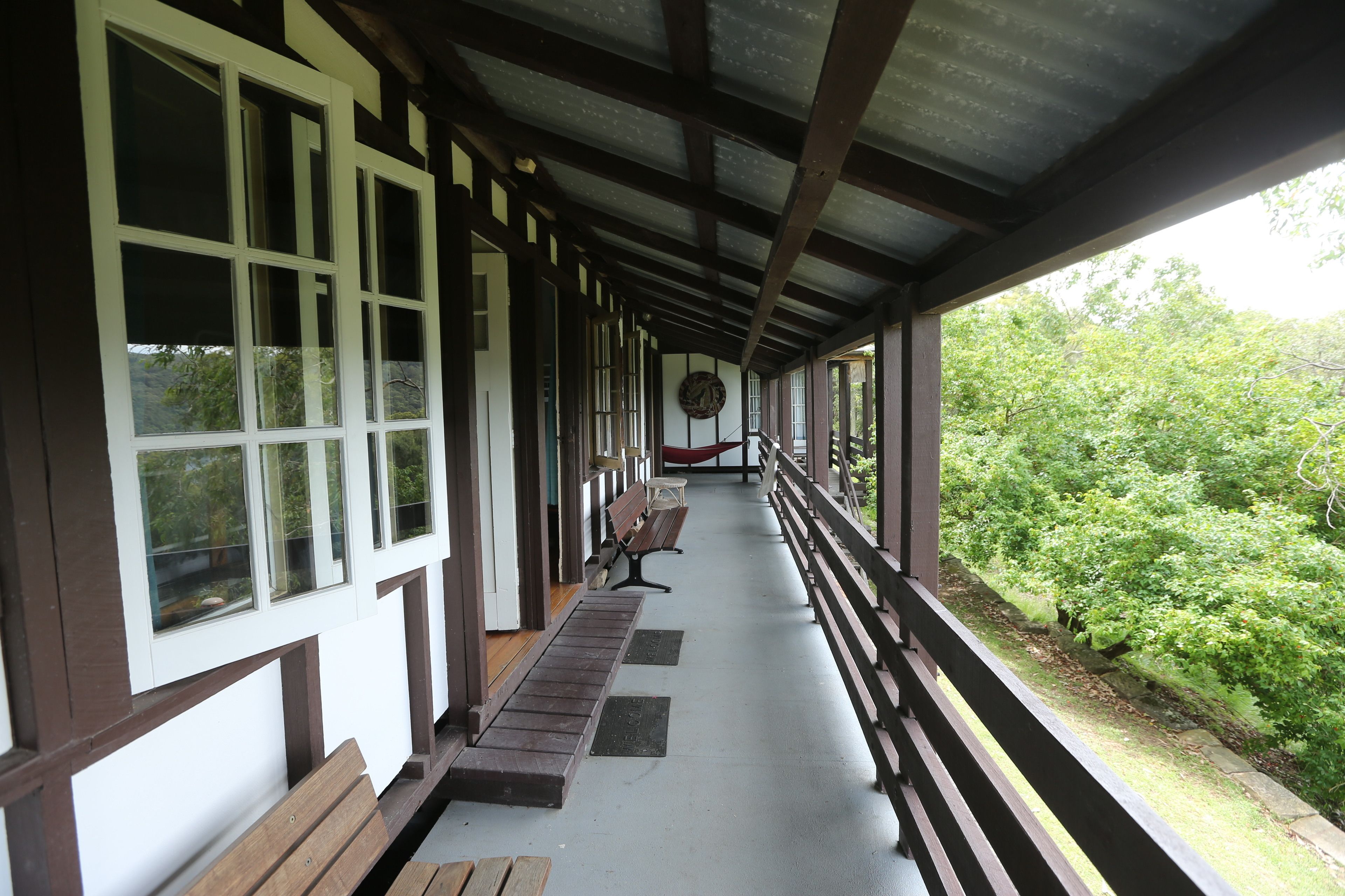 A covered porch with wooden benches and a railing, overlooking a lush green landscape.