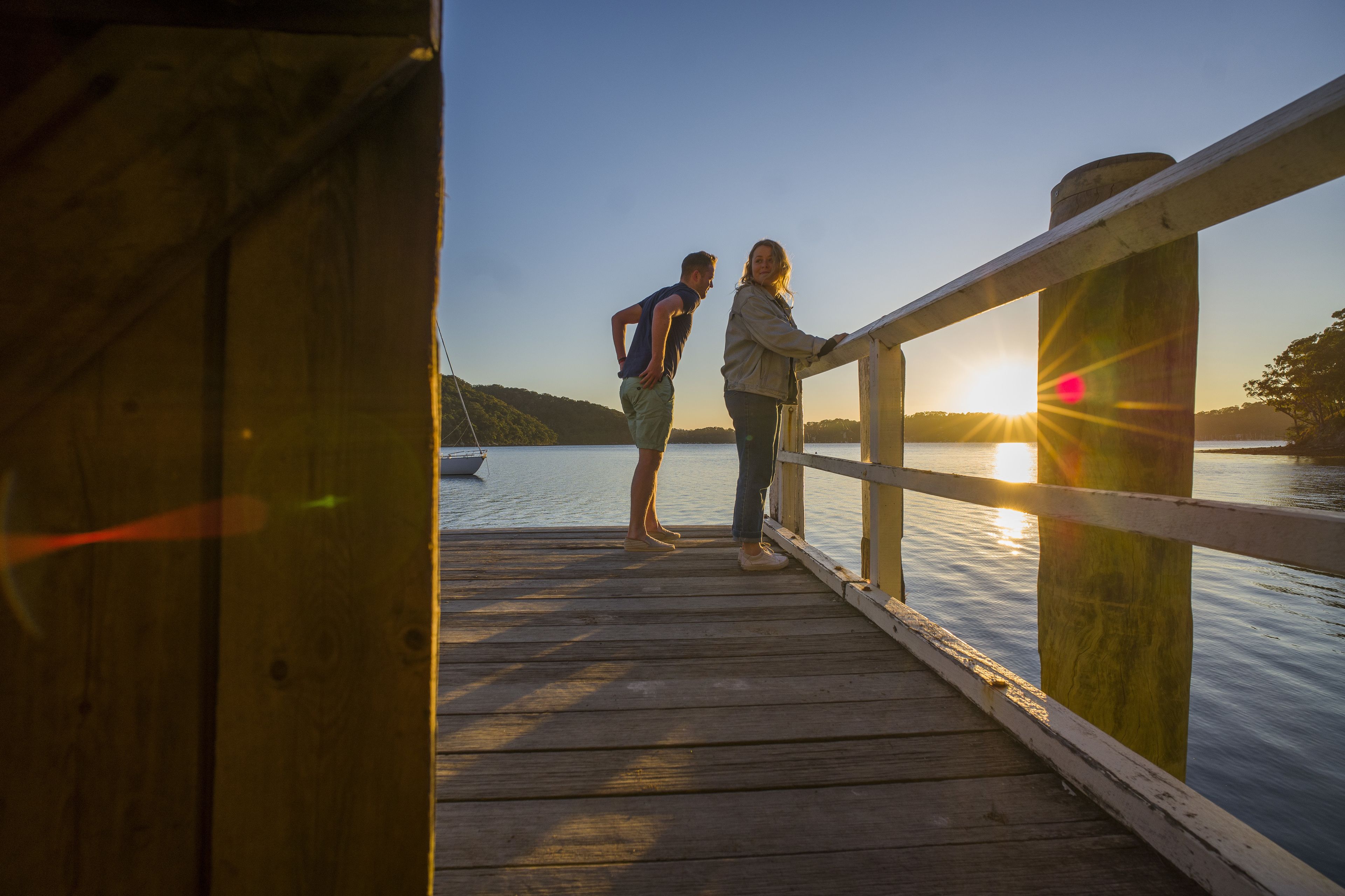 A wooden pier with a railing, overlooking a calm body of water and a sunset.