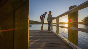 A wooden pier with a railing, overlooking a calm body of water and a sunset.