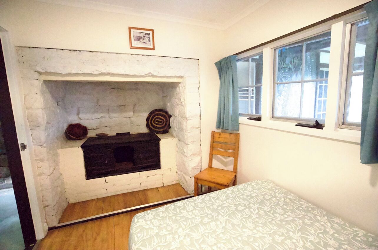 Una habitación con chimenea de ladrillo blanco, una silla de madera, una cama con ropa de cama estampada y una ventana con cortinas.