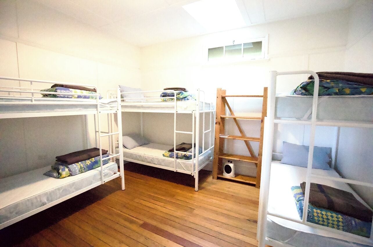 Une chambre de dortoir avec des lits superposés, une échelle en bois et une petite étagère.
