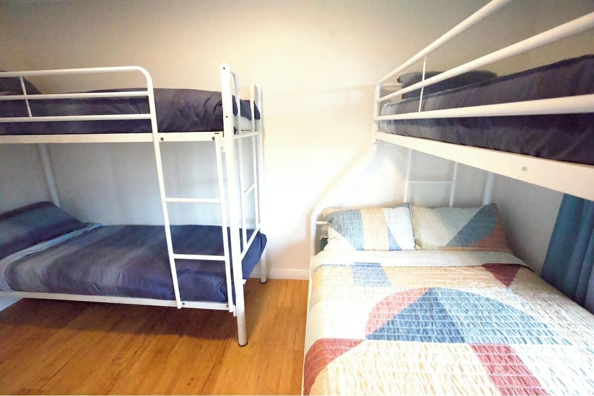 A room with two bunk beds, one with a blue and white striped bedspread and the other with a multicolored quilt.