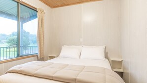 A bedroom with a large bed, two bedside tables, a window with a curtain, and a view of greenery outside. - NRMA Warrnambool Riverside Holiday Park (Allansford)
