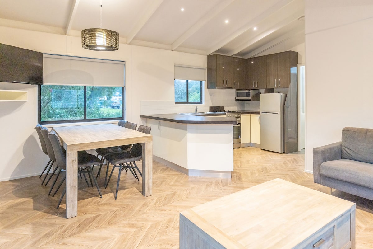 A modern kitchen with a large island, wooden flooring, and a dining area with chairs.
