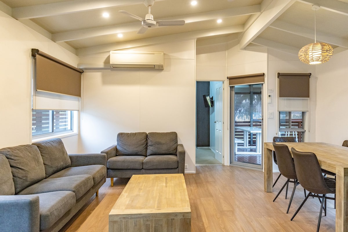 A modern living room with a grey sofa, a wooden coffee table, and a dining area with a wooden table and chairs.