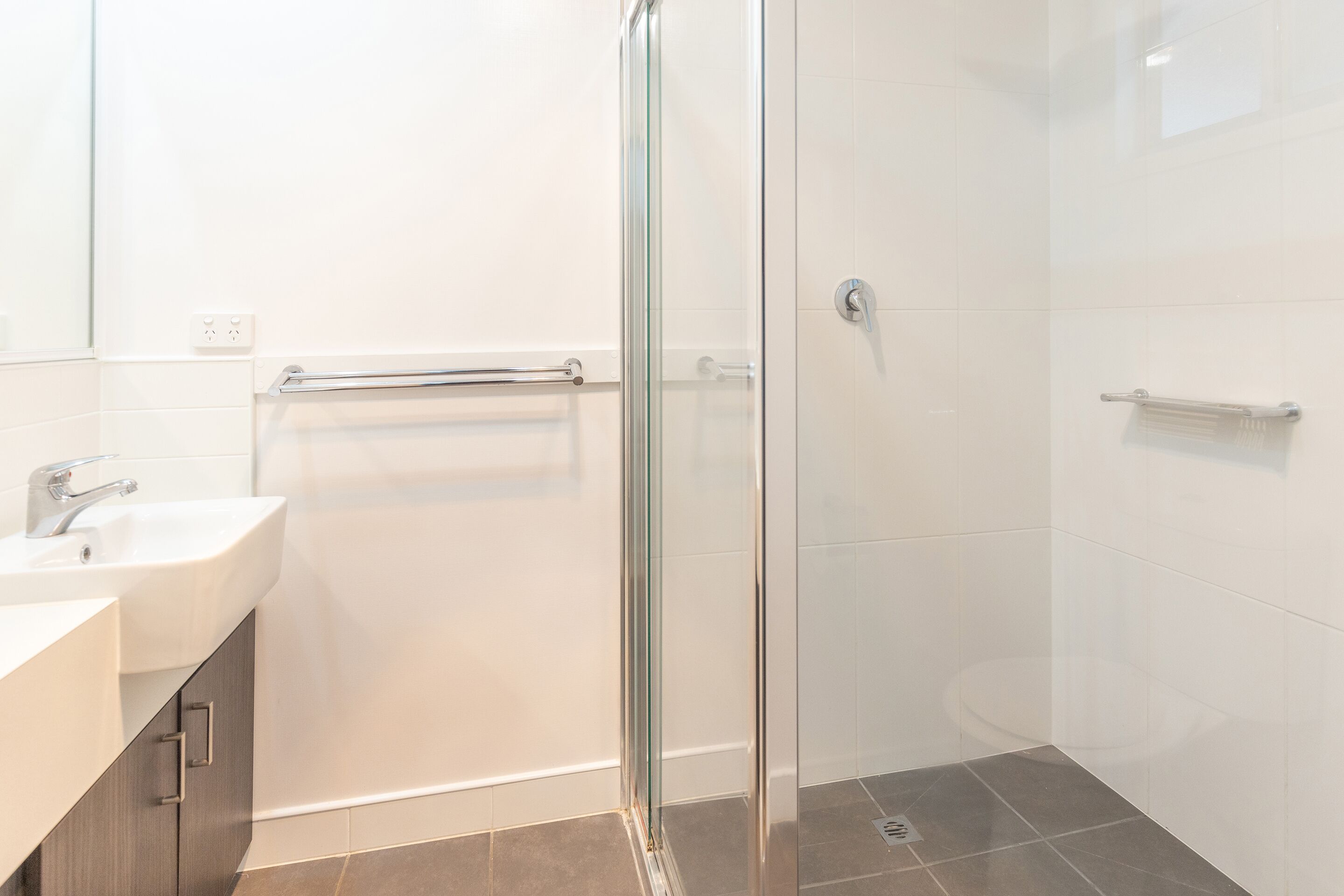 A modern bathroom with a glass shower enclosure, a white sink, and a towel rack.