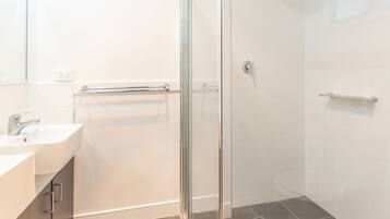 A modern bathroom with a glass shower enclosure, a white sink, and a towel rack.