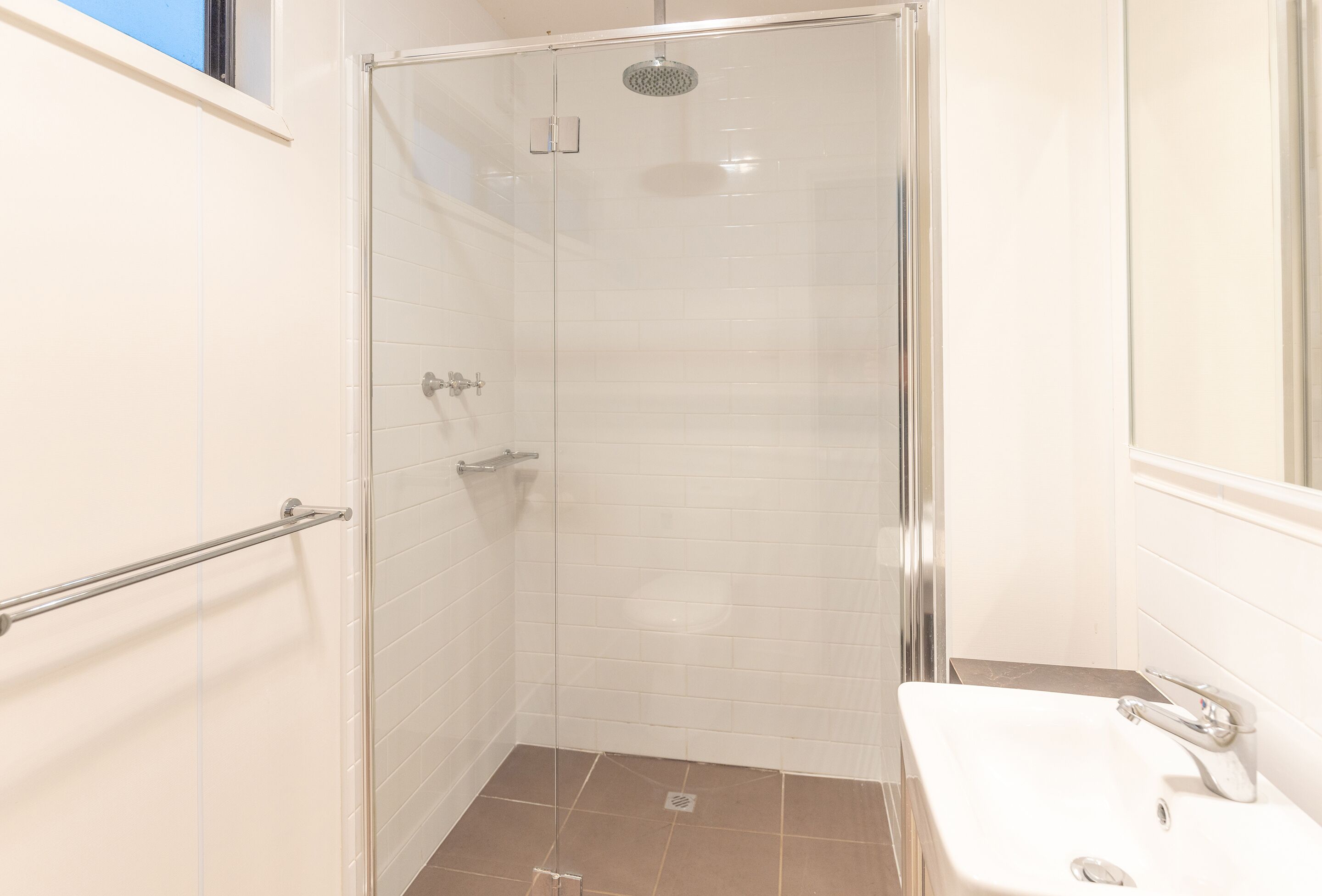 A modern bathroom with a glass shower enclosure, a white sink, and a tiled floor.