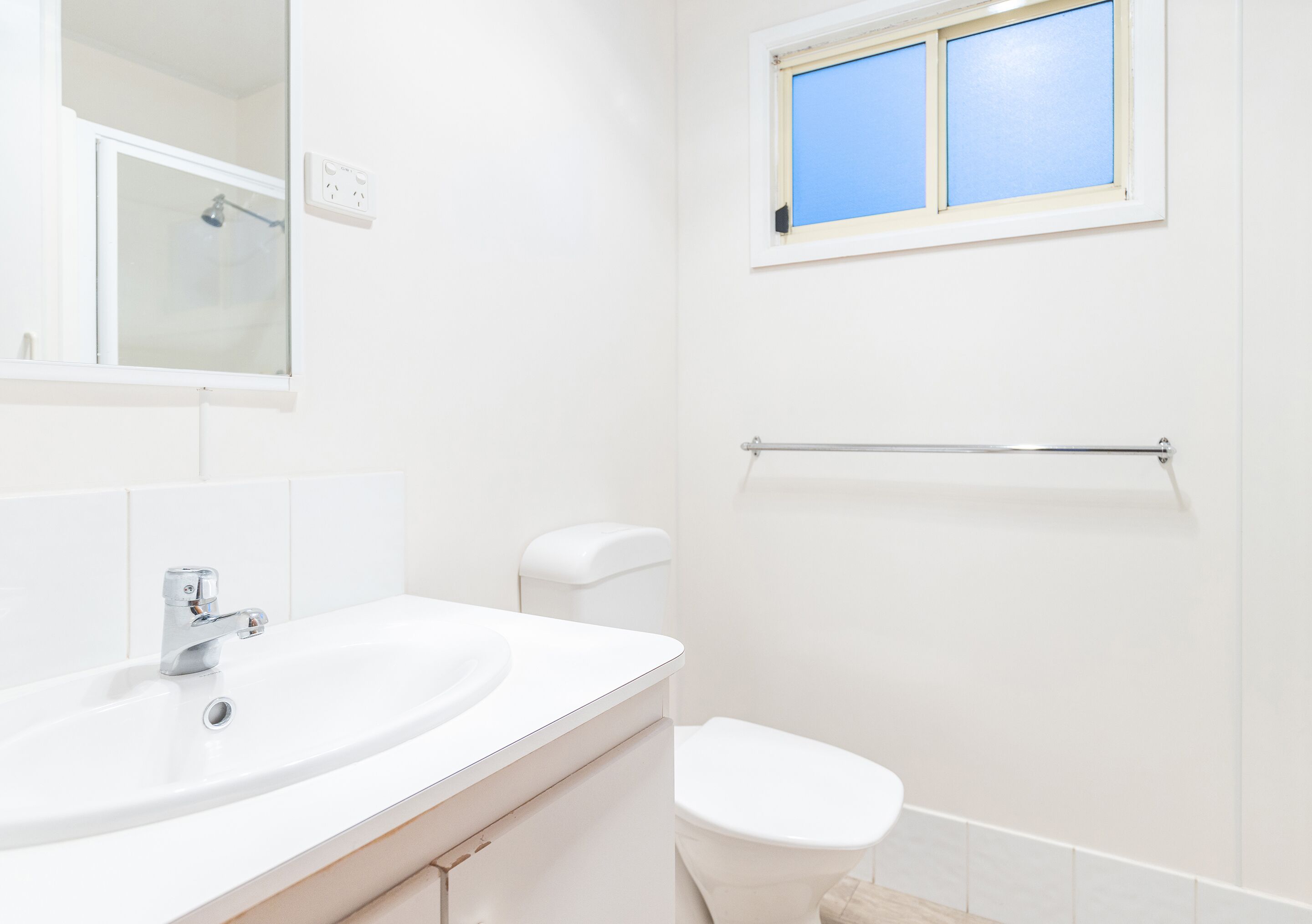 Un baño con un lavamanos blanco, un inodoro, una ventana y un perchero para toallas.