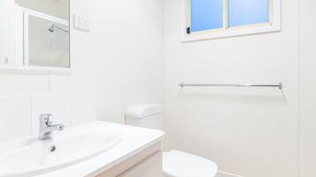 Un baño con un lavamanos blanco, un inodoro, una ventana y un perchero para toallas.