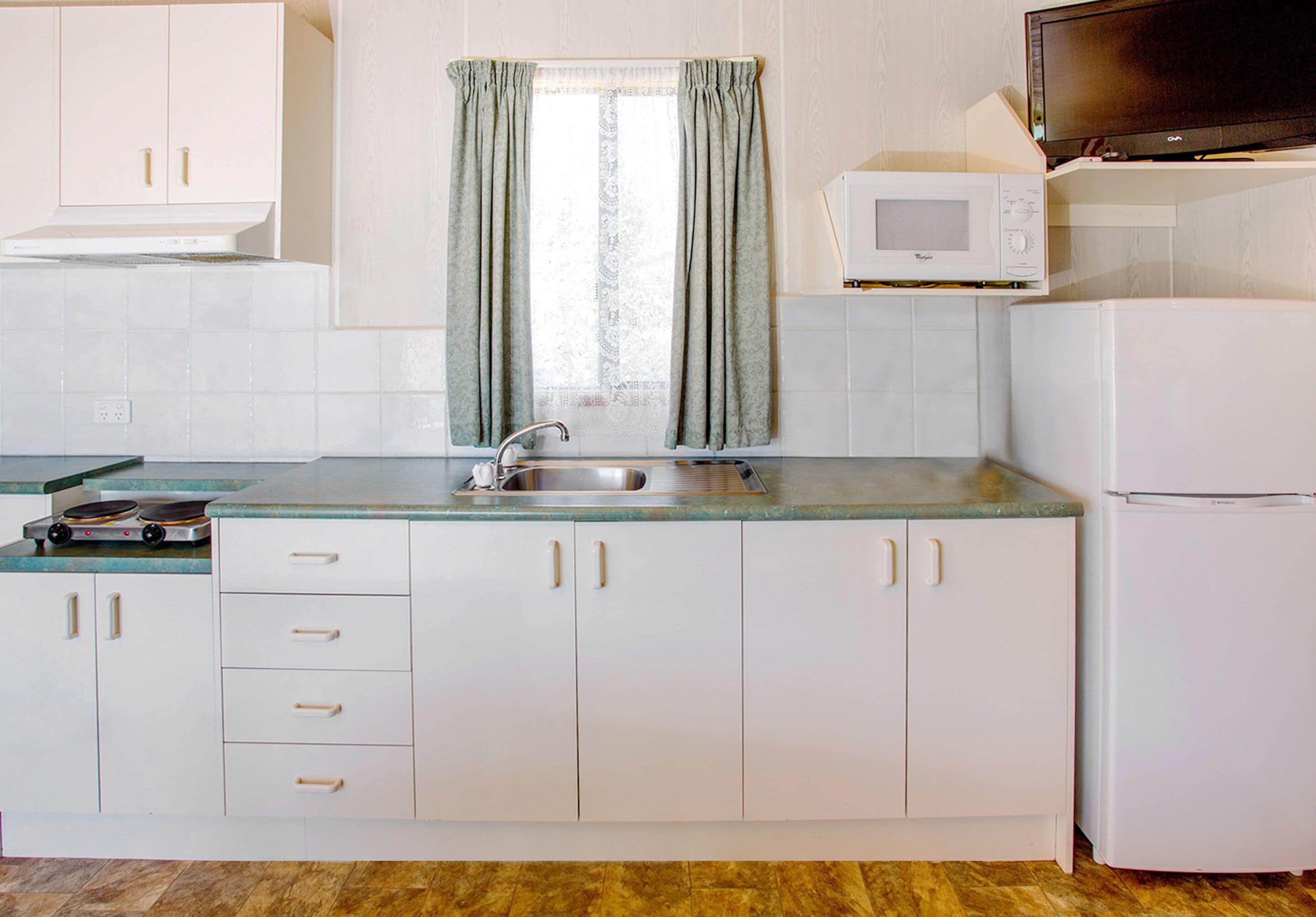 A kitchen with white cabinets, a stainless steel sink, a microwave, and a refrigerator.