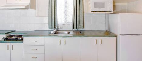 A kitchen with white cabinets, a stainless steel sink, a microwave, and a refrigerator.