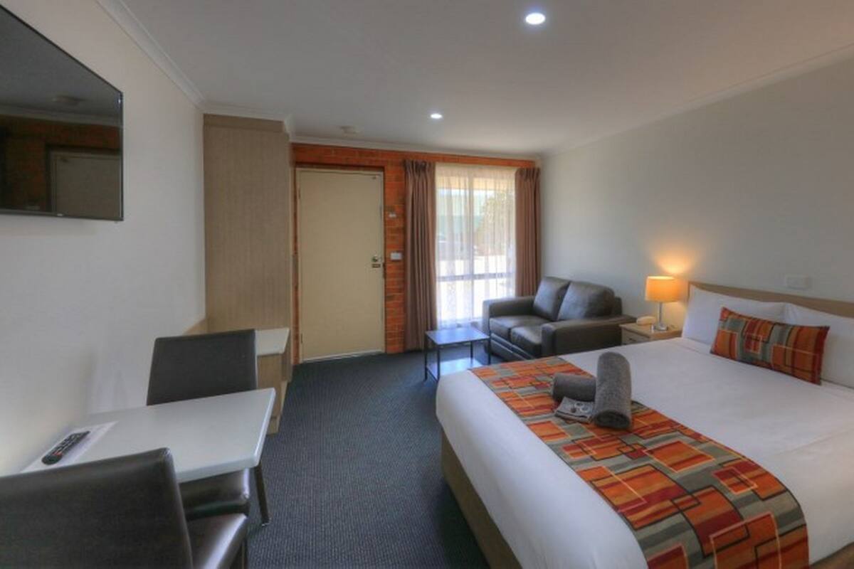 A hotel room with a bed, a desk, a chair, a sofa, and a TV.