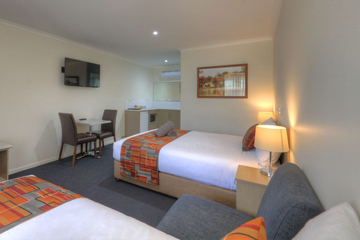 A hotel room with two beds, a desk, a chair, a small kitchenette, and a TV.