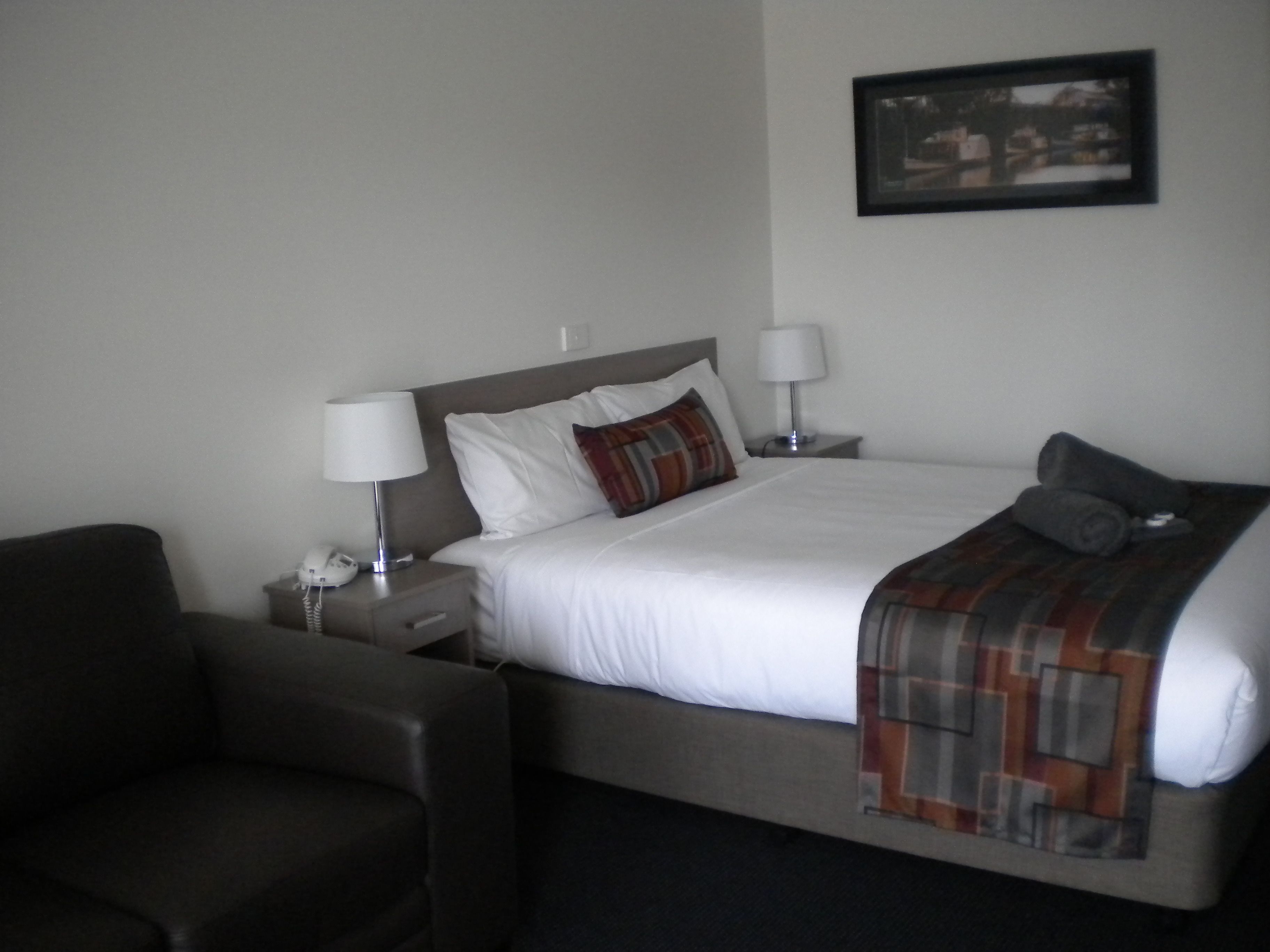 A neatly made bed with white linens, a plaid throw blanket, and two bedside lamps.