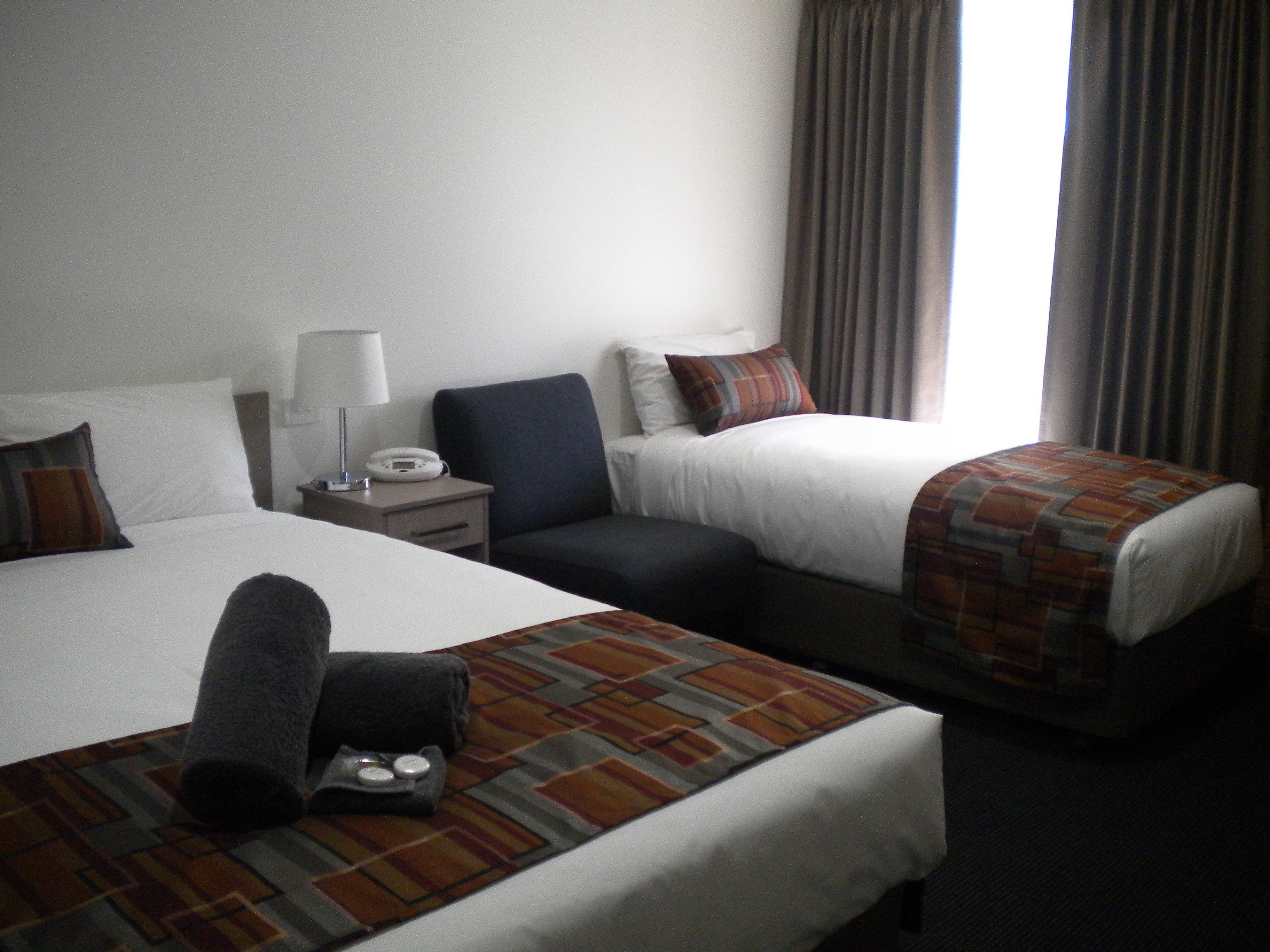 A hotel room with two beds, a nightstand with a lamp, a telephone, and a window with curtains.