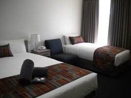 Una habitación de hotel con dos camas, una mesita de noche con lámpara, un teléfono y una ventana con cortinas.