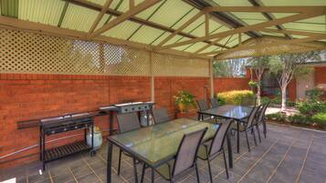 Un patio exterior con una parrilla, una mesa y sillas.