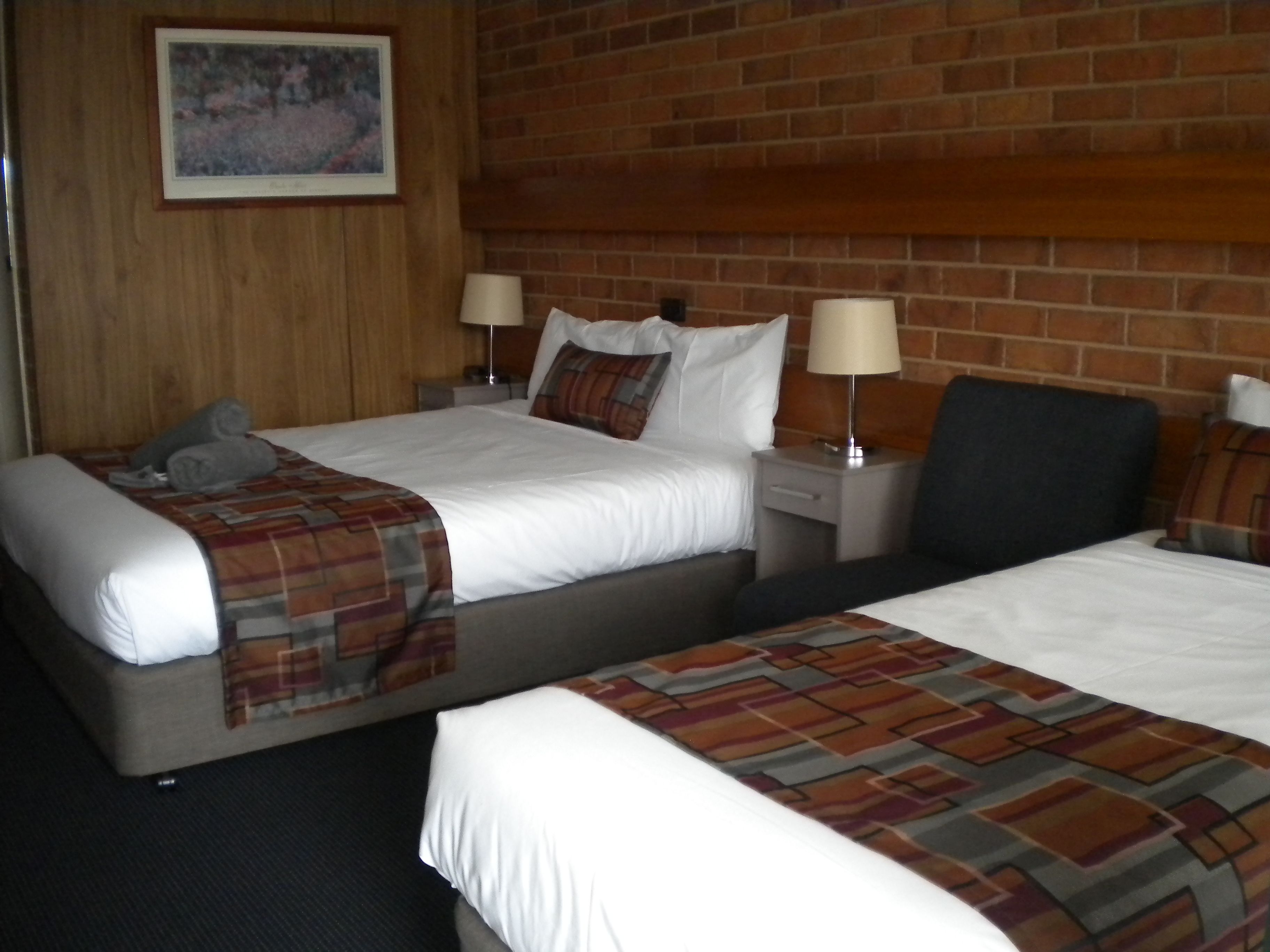A hotel room with two beds, a wooden headboard, a nightstand with a lamp, and a painting on the wall.