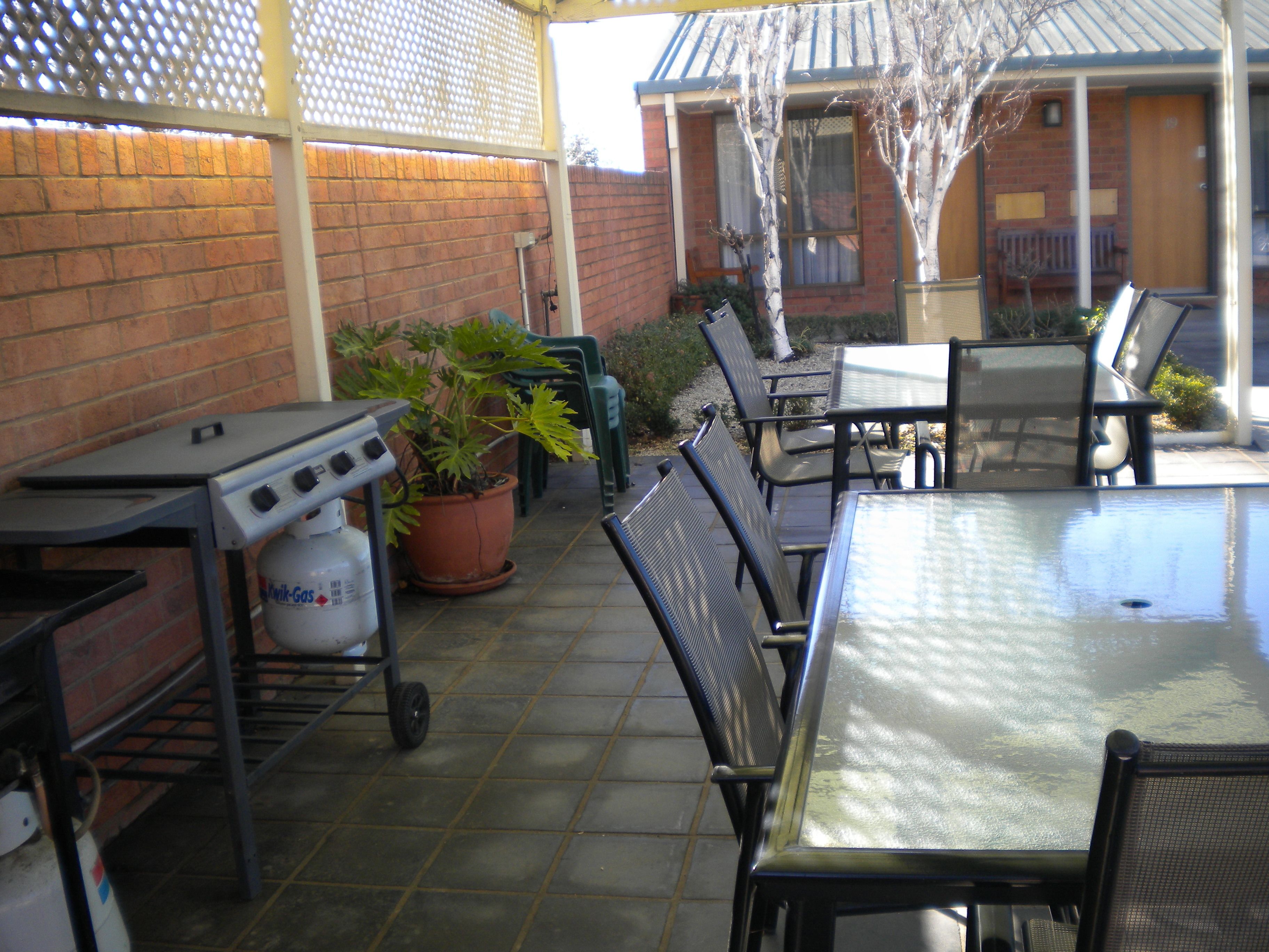 Une terrasse extérieure avec une table et des chaises, un barbecue et une plante en pot.