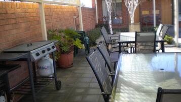 Une terrasse extérieure avec une table et des chaises, un barbecue et une plante en pot.