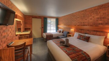 A hotel room with two beds, a desk, a chair, a TV, and a brick wall.