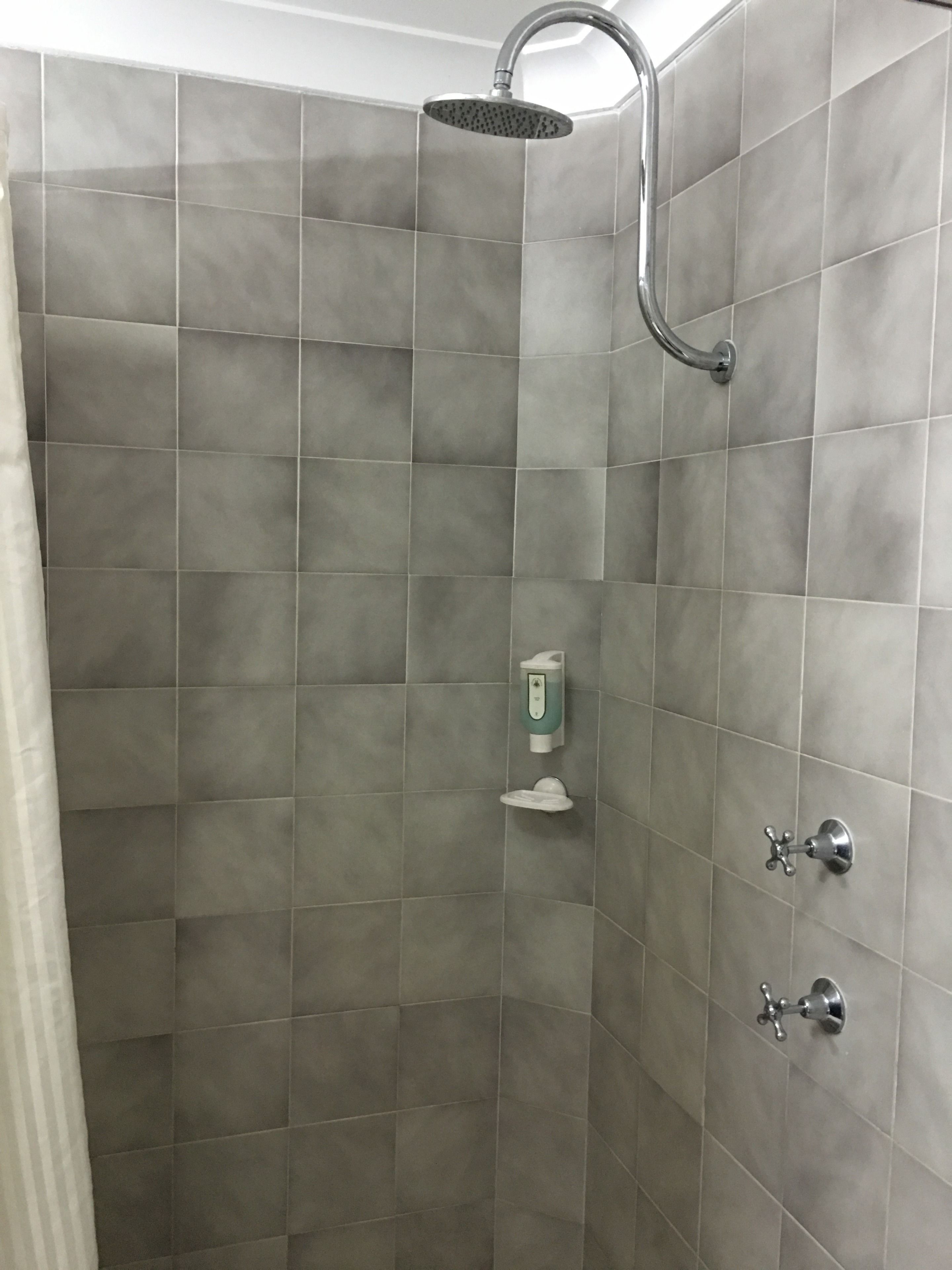A shower area with grey tiles, a handheld showerhead, a soap dispenser, and a wall-mounted faucet.